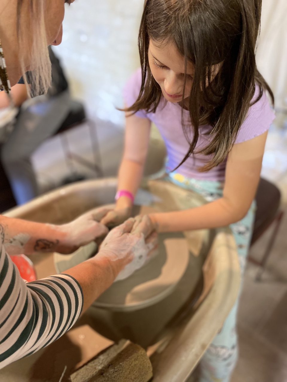 An artist guiding a child's hands at the pottery wheel